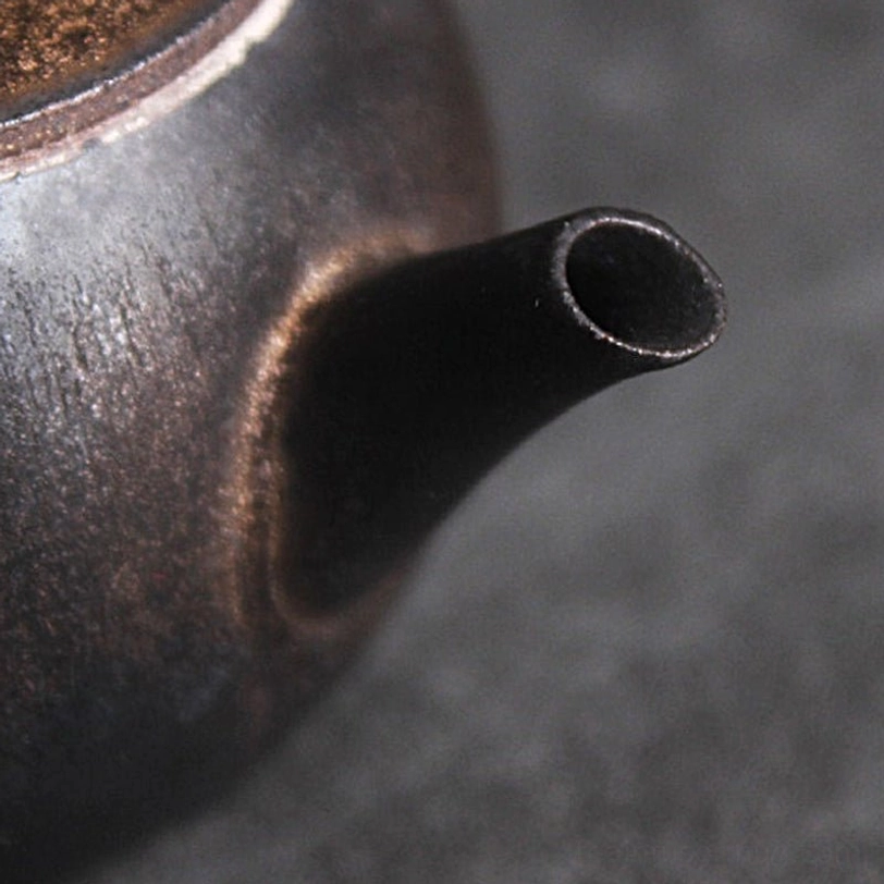 close up of slender smooth spout on black ceramic teapot