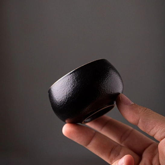 Side view of the textured black Japanese tea cup standing on matching saucer