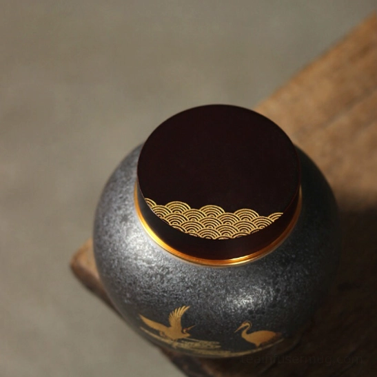 Side profile of deep grey tea storage canister showing golden crane motif