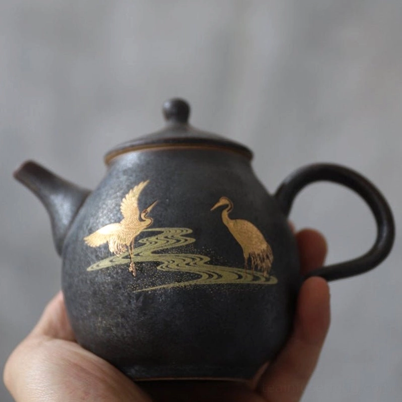 detailed close up of golden crane and water pattern on black ceramic teapot