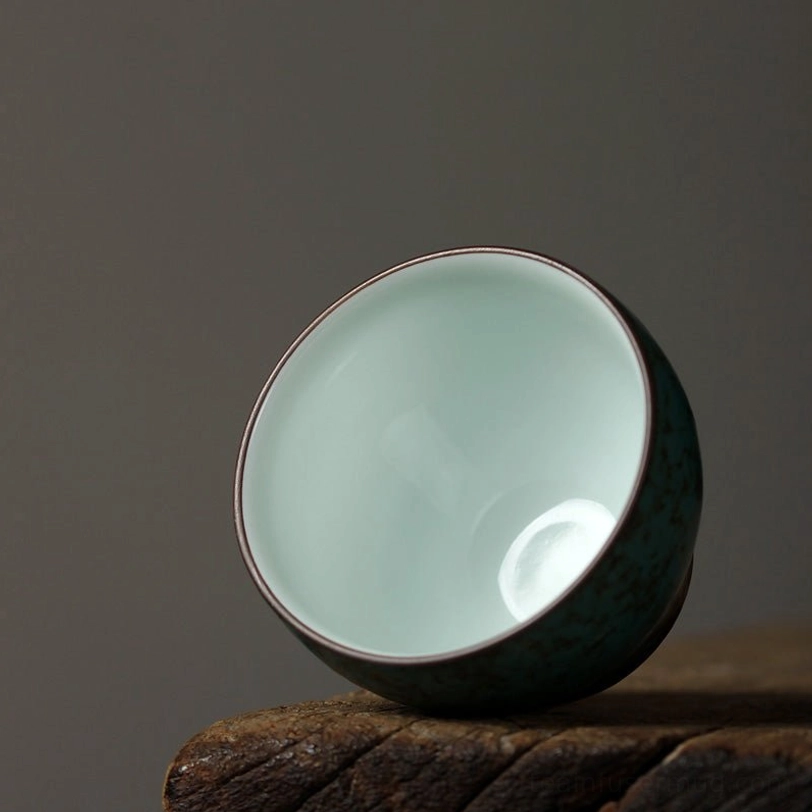 side profile of rounded green porcelain tea cup showing brown rim detail