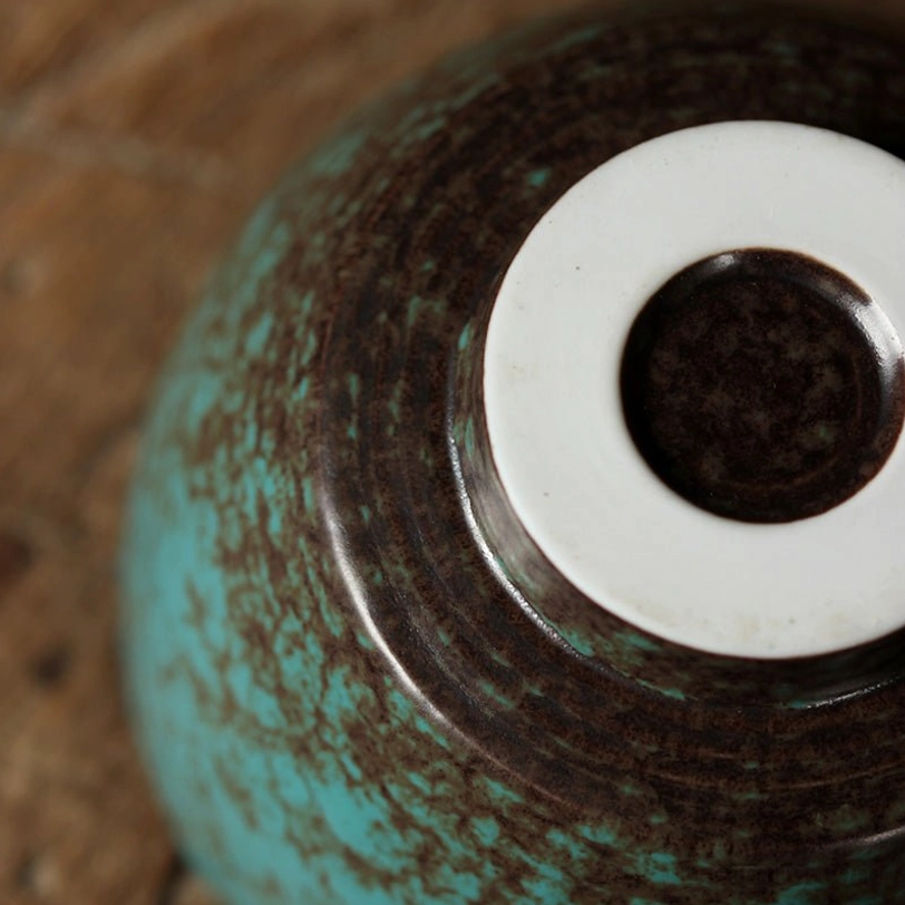 green porcelain tea cup alongside a small metal teaspoon for size reference