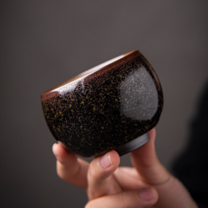 Handheld gold speckled Jian Zhan tea bowl held for size reference