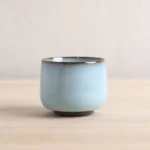 full side view of light blue ceramic Chinese tea cup with ancient coin base