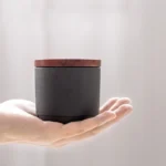 Hand holding small matte ceramic tea storage canister with wood lid