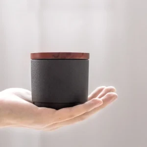 Hand holding small matte ceramic tea storage canister with wood lid