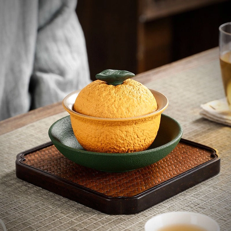 side view of orange citrus ceramic gaiwan tea cup with green saucer