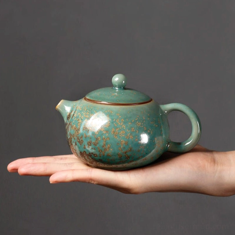side view of speckled glaze green ceramic teapot with infuser