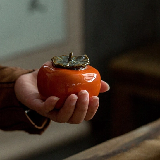 Hand holding small persimmon tea storage canister to show compact size