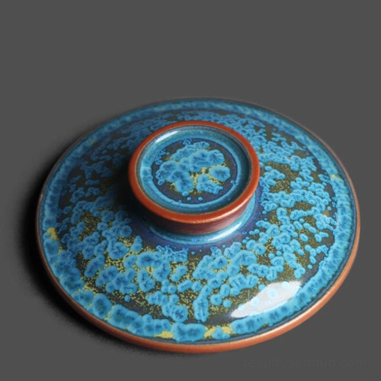 ceramic tea infuser resting on lid beside the blue speckled tea infuser mug