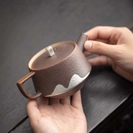 side view of textured brown ceramic teapot with faraway mountain motif